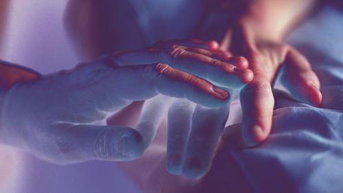 Una mano descansando sobre otra en penumbra azulada
