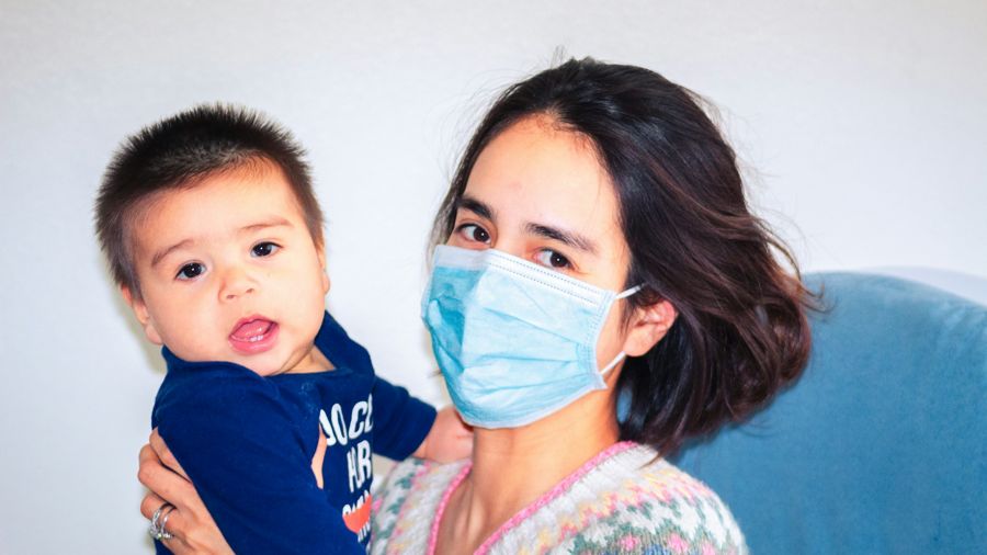 A woman in a surgical mask holding a baby whose mouth is open, as if about to speak