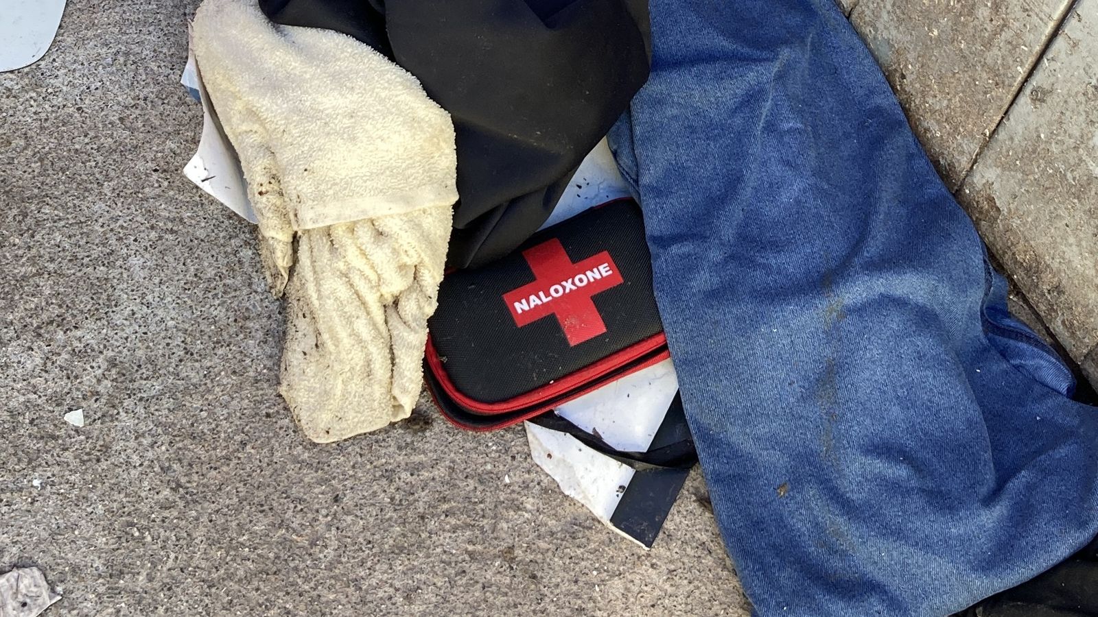 A naloxone kit, used to reverse opioid overdoses, lying among abandoned clothes in a Toronto alley
