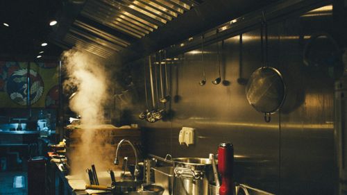 a mop leaning on a yellow bucket in an empty industrial kitchen, lights still on