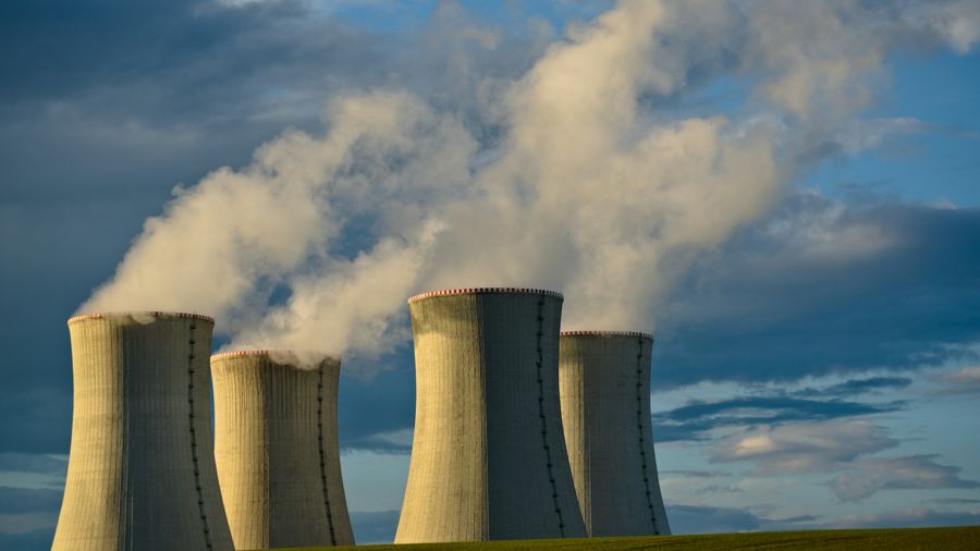 Four concrete cooling towers releasing steam under a blue sky with clouds