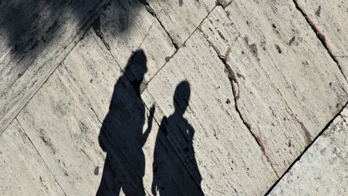 a shadow of two people walking down a sidewalk