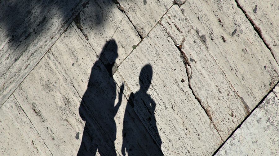 a shadow of two people walking down a sidewalk