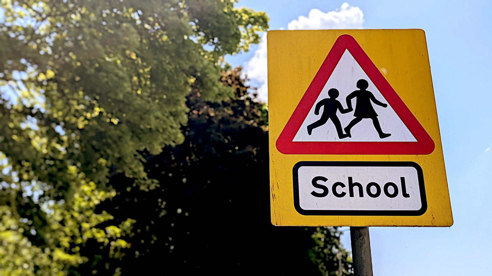 A yellow road sign warning of a school, with the silhouettes of two children