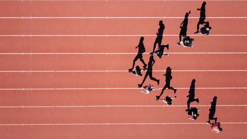 Corredores vistos desde arriba en una pista de atletismo, con sus sombras alargadas sobre las calles