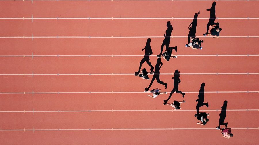 Corredores vistos desde arriba en una pista de atletismo, con sus sombras alargadas sobre las calles